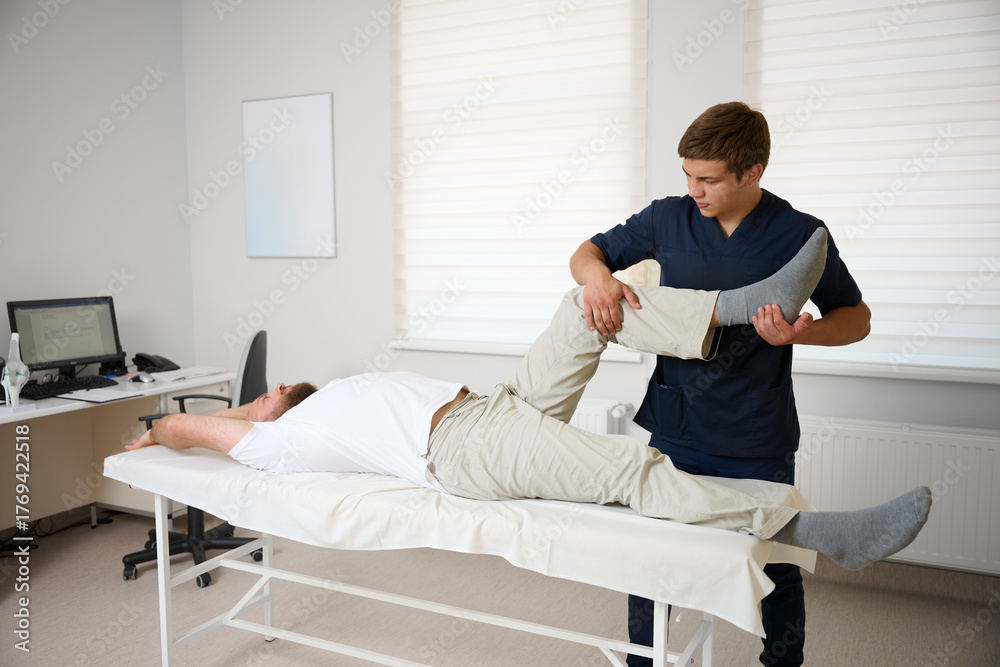 Obraz premium Physiotherapist examining patient knee joint during rehabilitation therapy session in modern medical clinic. Man receiving orthopedic treatment and physical therapy for injury recovery.