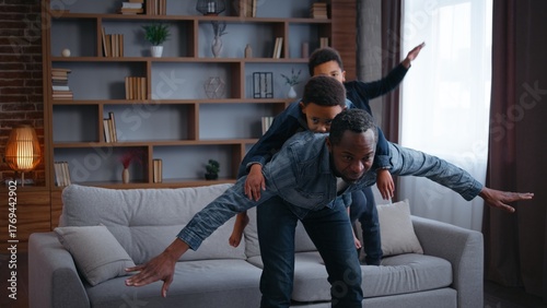Tableau sur toile Carefree African American family playing piggyback pretending airplane at home j
