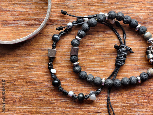 Close-up of handmade black bead bracelets with metal accents on a wooden surface. Minimal and natural jewelry style for product display, craft design, and fashion accessories concepts.