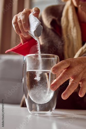 Foto Elderly woman pouring soluble powder from sachet into glass of hot water