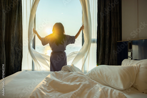 Bild auf Leinwand Confident middle aged woman opens the curtains with white flying curtains, looking at the view from window Beautiful sunrise above sea or ocean