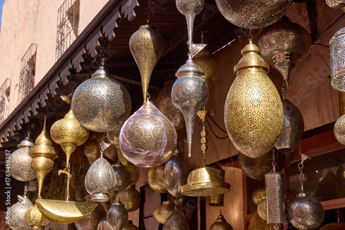 Numerous metal Moroccan lanterns hang from a building's awning. These traditional lanterns are silver and gold and cast beautiful shadows. Located in Morocco