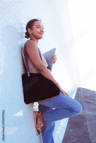 Young woman standing outdoors holding laptop thinking