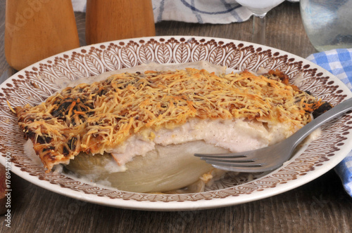 Assiette d'endive au jambon gratinée maison avec une fourchette servie à table en gros plan