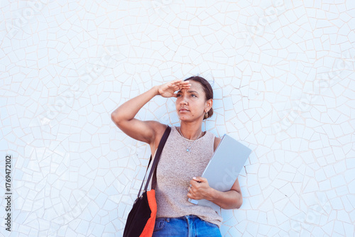 Woman looking forward shielding eyes holding laptop