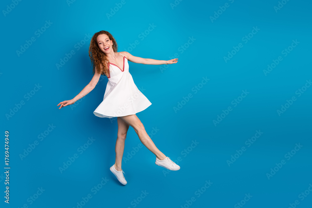 Obraz premium Joyful young woman in white dress jumps against blue background for lifestyle fashion promotion