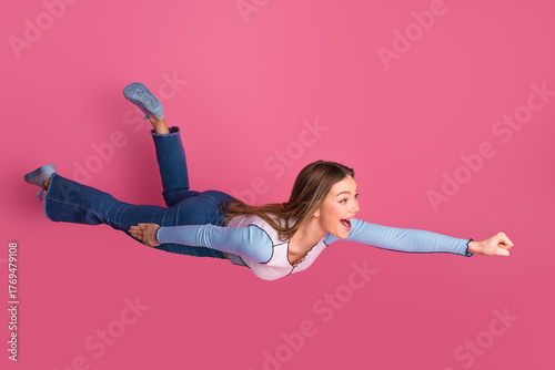 Charming young woman playfully mimics flying superhero pose against vibrant pink background embodying fun joy and youthful spirit