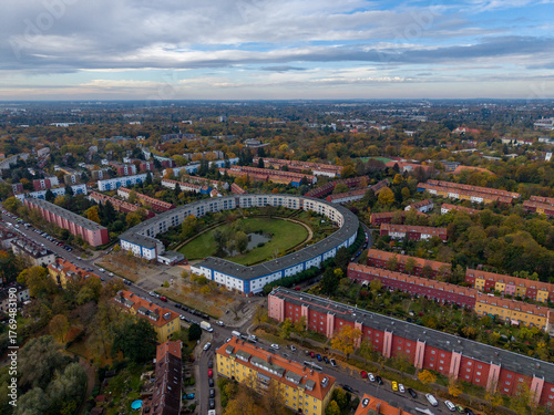 Aerial view of a semicircular building complex nestles amidst a tapestry of autumnal trees, a mosaic of terracotta roofs and verdant parks, Berlin, Berlin, Germany.