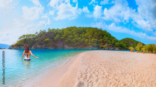 Fototapeta Naklejka Na Ścianę i Meble -  Beautiful young woman in a dark blue  bikini standing on the beach looking at the sea - Ölüdeniz beach and blue lagoon, best beaches in Turkey - Fethiye