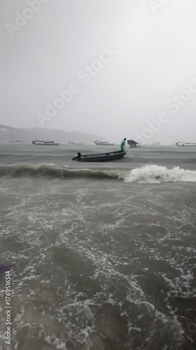 Person bails water from a small vessel as it's buffeted by choppy waves near the shore on a stormy day.