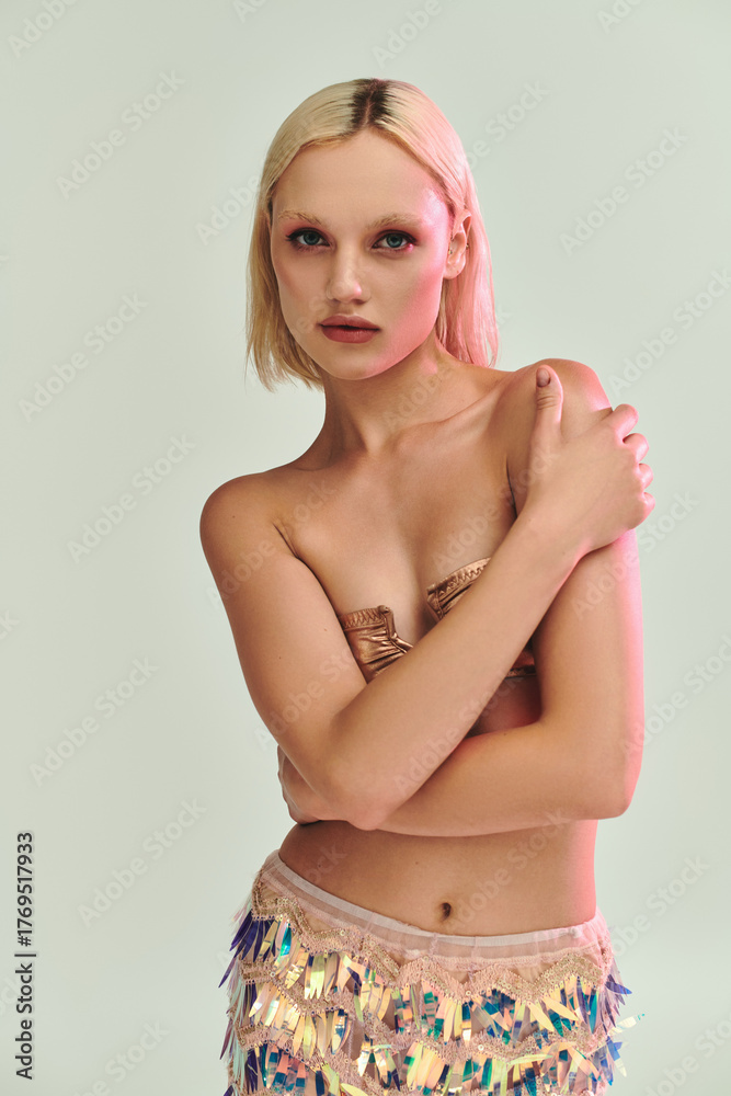 Naklejka premium Blonde young woman showcases stylish holographic party look in studio setting