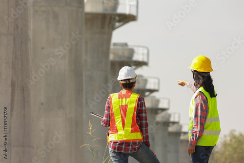 Two construction workers communicate on-site, discussing project elements while wearing safety gear and helmets.
