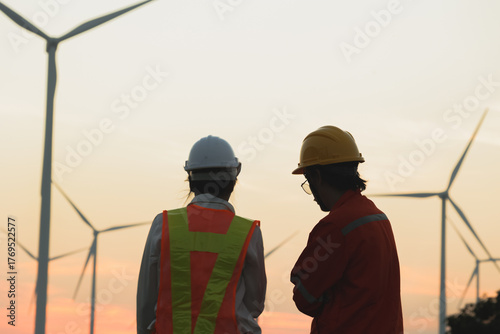 Two workers discuss renewable energy projects at a wind farm during sunset, showcasing dedication to sustainable solutions.