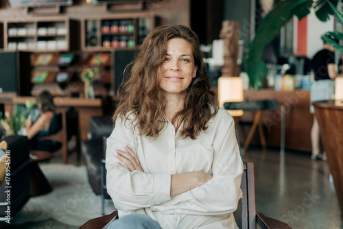 Confident woman sits in a cozy cafe with arms crossed, smile and look at the camera