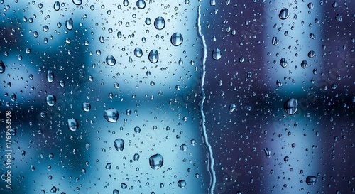 Raindrops on a glass window with blurry blue background.