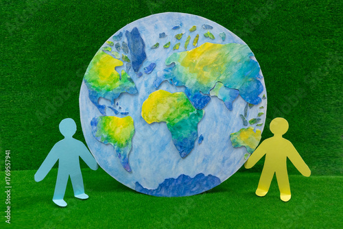 Next to beautiful model of planet Earth on green grass background are figurines of little people.
