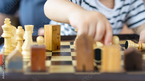 Child playing chess with wooden house models, representing real estate education, inheritance planning, legacy transfer, future investment, and building family wealth.