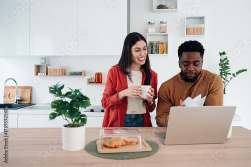 Diverse couple managing finances online in kitchen