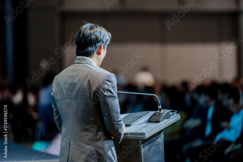Rear view of man speaker giving an inspiring talk or leading a workshop for young professionals and adult training participants in a large conference room.