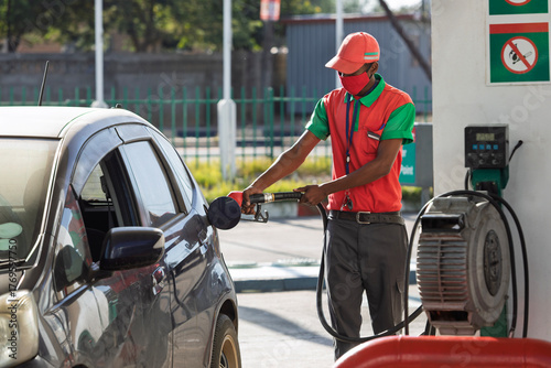 African attendant at a petrol station filling a car with gas petrol, pump in hand