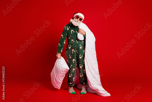 Playful Santa in festive pajama with blanket and pillow against a bold red backdrop