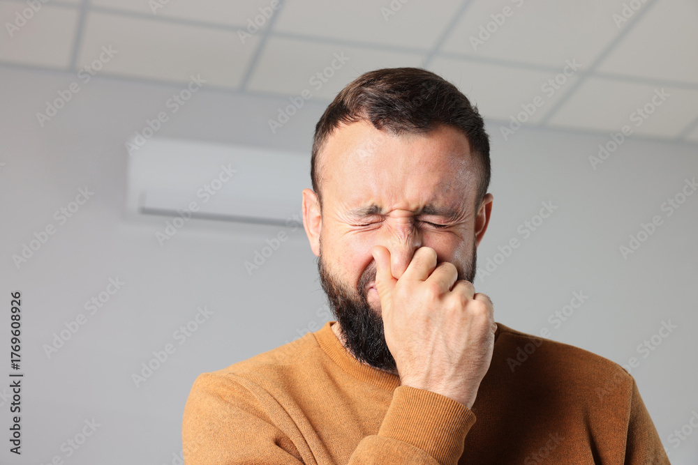 Obraz premium Man feeling bad smell from air conditioner indoors, space for text