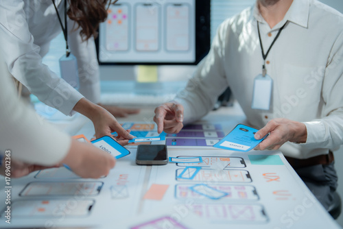 UX designers collaborating at an office table, discussing mobile app wireframes and user interface prototypes to plan the next phase of development