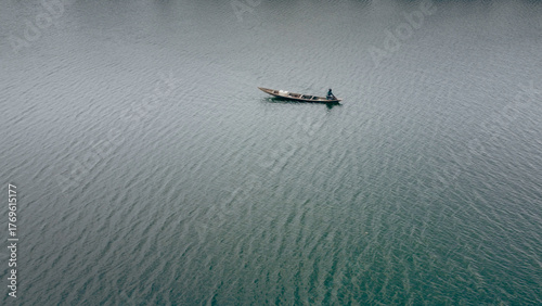 Aerial view of a lone boat slicing through the tranquil, rippling waters, a dark silhouette against the shimmering expanse, Abuja, Federal Capital Territory, Nigeria.