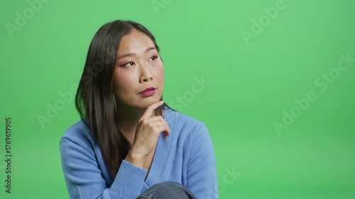 Young woman with eyes closed rests chin on hand against green background.