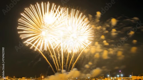 Spectacular golden fireworks explode in the night sky above a distant city skyline creating a