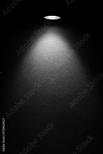 Single spotlight on a dark textured wall with a cone beam and soft vignette. Minimal versatile background with room for headline or logo.