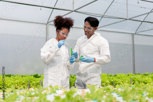 Two people in lab coats are working on a project in a greenhouse