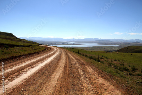Dirt roads in the QwaQwa villages, located in the mountainous region of the Free State province in South Africa. Trees and plants like Wild Dagga in the foreground. Mountains in the background. 