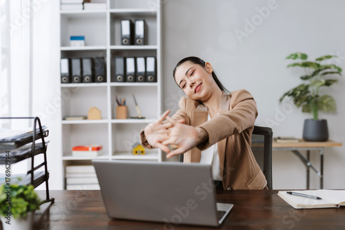 Asian businesswoman doing office stretches at her desk, feeling relaxed during a busy workday or break