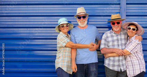Obraz na plátne Group of happy senior friends enjoying time together outdoors, smiling and hugging in front of a blue metal wall