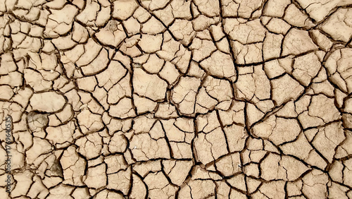 Cracked earth under the scorching sun, a sign of drought and arid conditions. The parched ground displays a network of fissures, reflecting the harsh environment