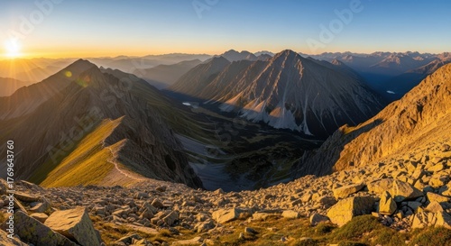 Golden sunrise illuminates rugged mountain range with deep valley and clear blue sky