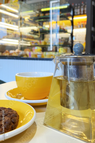A yellow cup and teapot with tea are on the cafe table. Blurred background of the cafe interior.Vertical 