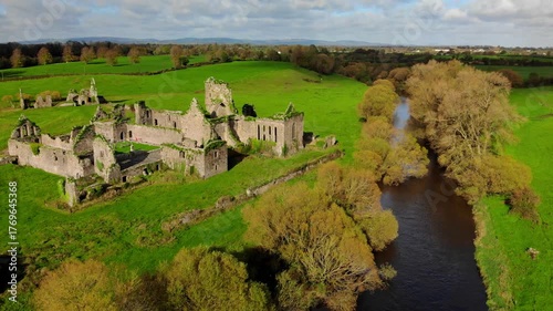 Explore ancient ruins beside a peaceful river in the lush green countryside of Ireland on a sunny afternoon