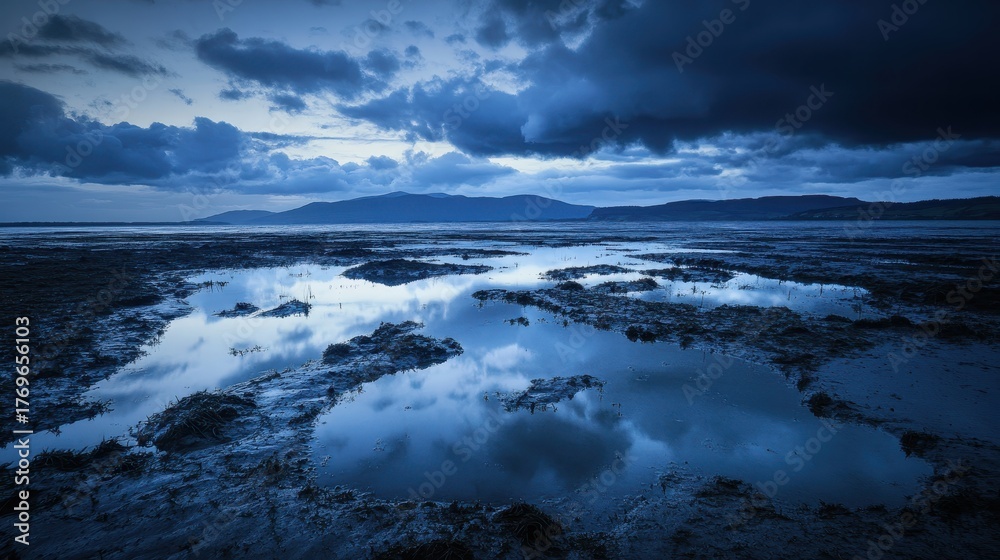 Obraz premium Rippling lake water reflecting mountains under dramatic clouds