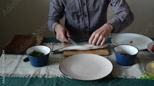 A man begins to cut up a sea bass, cutting off its fins.