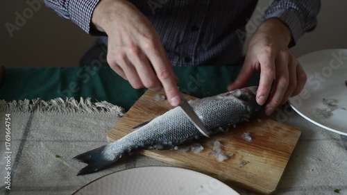 A man cleans fish from scales with a knife