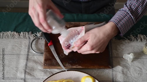 A man is salting gutted sea bass fish and adding other spices