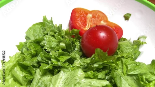 A plate of lettuce and a tomato drops pieces of sliced sweet red pepper. Vegan food.