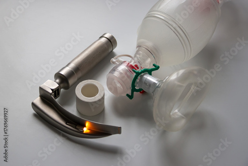 A laryngoscope, adhesive plaster and an Ambu breathing bag are on a white table. Horizontal shot.