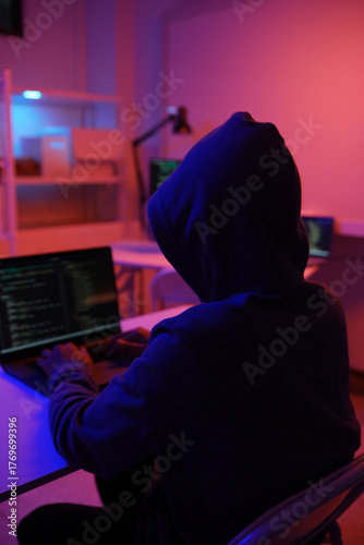 A mysterious hooded hacker working on a computer in a dark room.