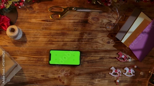 Top view of a Christmas gift wrapping scene with ribbons, scissors, paint, and homemade decorations on a rustic wooden table. Festive background for DIY holiday preparations with space for text.