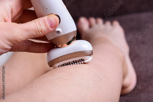 Schilderij op canvas A young woman removes her leg hair using an electric epilator at home