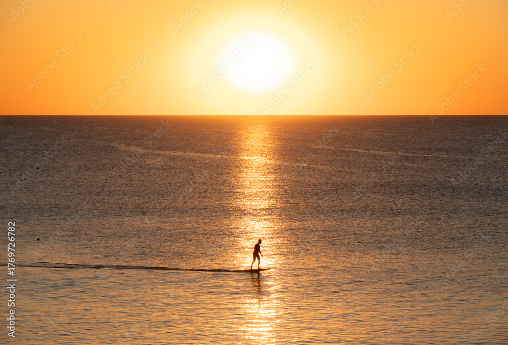 Fototapeta premium A serene silhouette of a paddleboarder glides across calm ocean waters during a golden Florida sunrise at South Ponte Vedra Beach