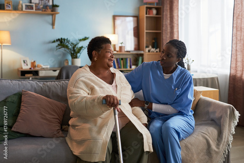 Принти на полотні Senior Black woman sitting on sofa holding cane, talking with young adult Black
